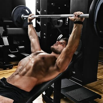 shirtless man lifting weights seated on a bench