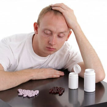 man frustrated over bottle of pills in front of him