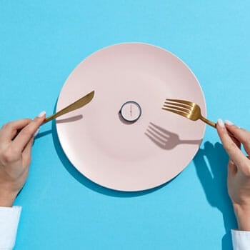 plate with small clock on it and a person holding knife and fork