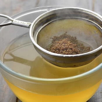 ajwain on a strainer and a bowl of ajwain water