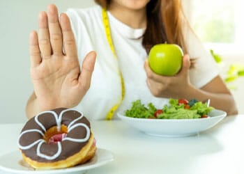 woman holding an apple while saying no to donuts