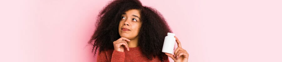 woman thinking while holding a capsule bottle