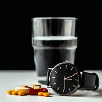 A watch, a glass of water and different supplements on a table