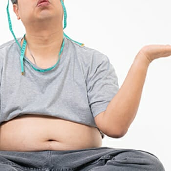 Guy sitting with belly out and measuring tape wrapped around his neck