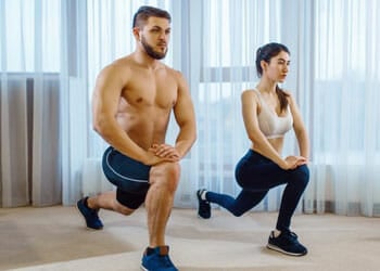 man and woman doing lunges together in gym clothes