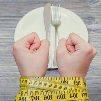 empty plate on a table and a person hand tied in a measuring tape