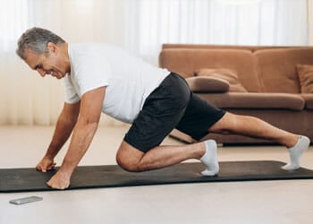 old man doing lunges in a yoga mat indoors