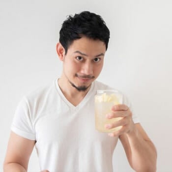 man in a white shirt holding up a glass of lemon water