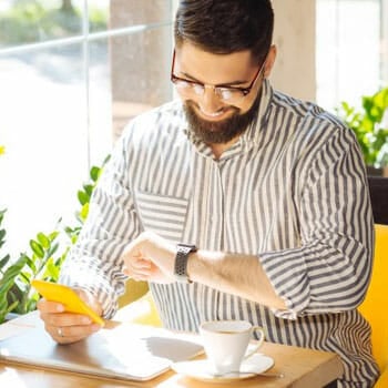 man sitting in a cafe looking at his watch while holding his phone