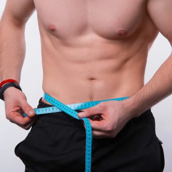 shirtless man using a measuring tape on his abs