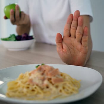 person's hand shoving away a pasta plate