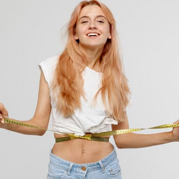 woman smiling in a crop top with her waist cinched in a measuring tape
