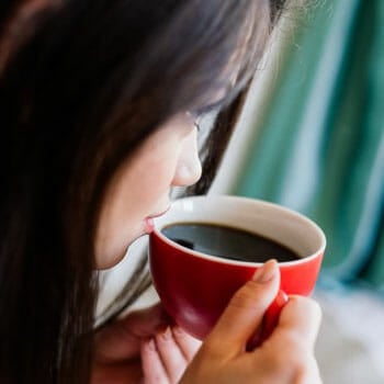 woman sipping coffee from a red mug