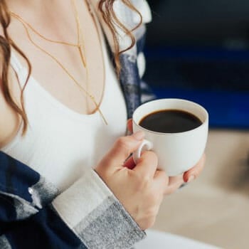 close up image of a woman's hand holding a white coffee mug