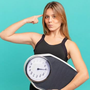 woman thinking with her hands pointing to her head while holding a weighing scale