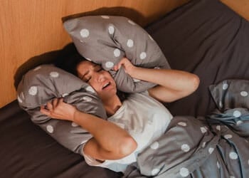 woman covering her ears with pillows in frustration