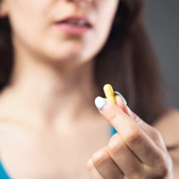 woman holding up a single yellow pill