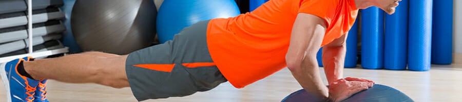 A man in orange shirt doing a push-up on a bosu