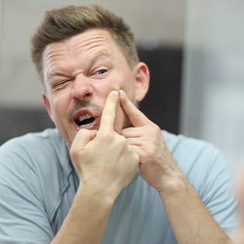 man facing the mirror and popping a pimple