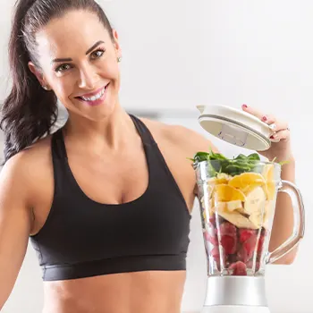woman in gym clothes using a blender smiling