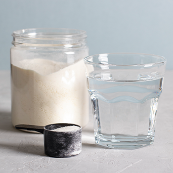 glass of water with a jar of powder and scooper