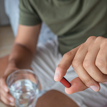 man holding up a red capsule and a glass of water