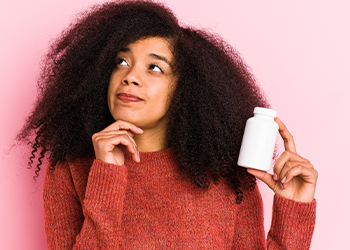 woman holding up a capsule bottle while thinking