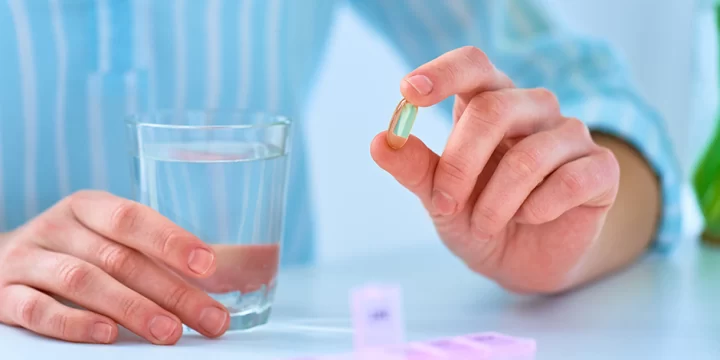 A person holding a supplement and a glass of water