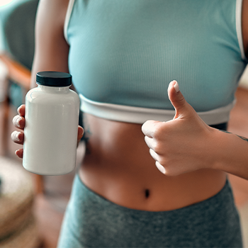 woman in gym clothes holding up a container and her thumbs up