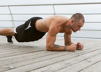 shirtless man doing planks outdoors