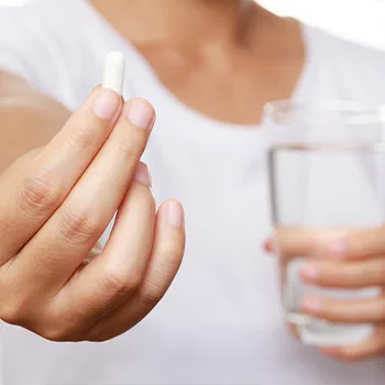 hand view of a person offering a white pill and glass of water