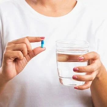 Woman holding a pill and a glass of water