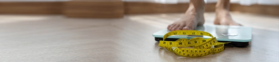 feet view of a person on a weighing scale with tape measure