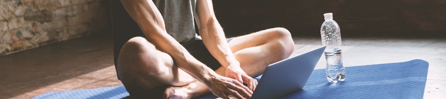 A person sitting on the floor on a yoga mat using a laptop