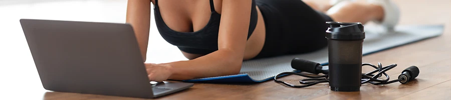 Woman in fitness attire using her laptop on the floor