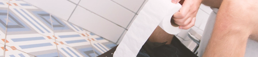 A man holding a toilet paper roll while sitting on the toilet