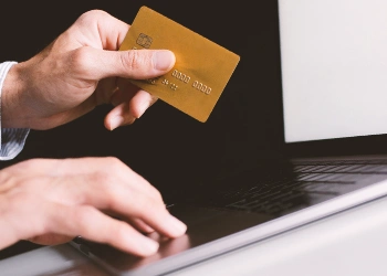 A man holding a credit card in front of the laptop