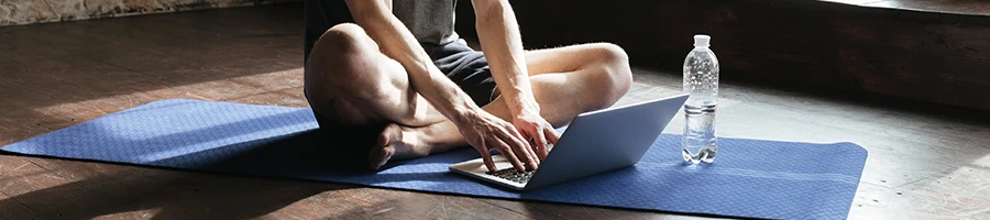 Man in yoga mat using laptop