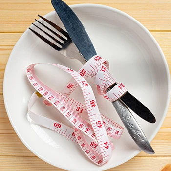 An empty plate with spoon and fork and measuring tape