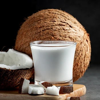 A glass of coconut milk in front of a coconut
