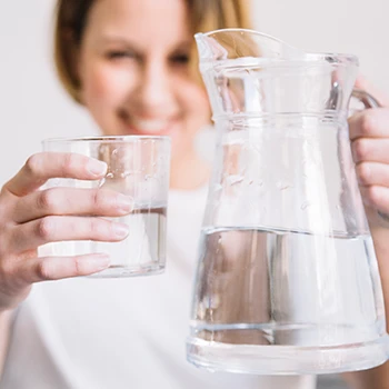 A woman showing a glass of water and a pitcher