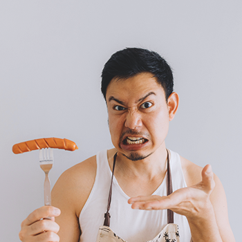 A buff male holding a sausage on a fork with an angry face