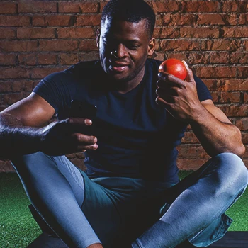 A 40 year old buff male holding an apple while looking at the phone