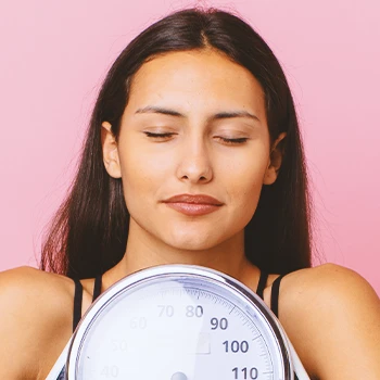 A woman holding a weighing scale near her face