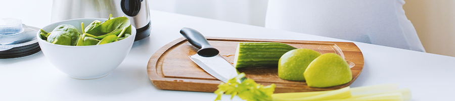 Cucumber and lime on a chopping board with a knife and a bowl of vegetables on the side