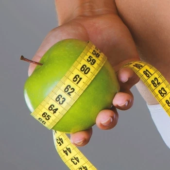 A person holding a measuring tape and an apple