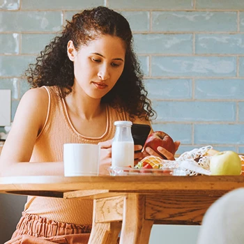 A person looking at her phone in the kitchen while holding an apple