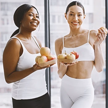 Two fit women holding apples side by side
