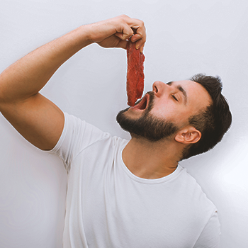 A bearded man holding steak up to his mouth