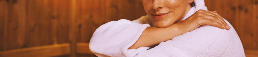 A woman posing for the camera with a towel robe on inside a sauna